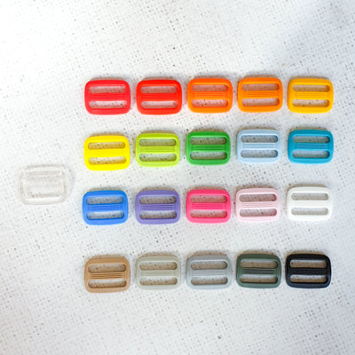 Assorted colourful plastic buckles on a textured white background. KAM Plastic Slider 25mm – Durable adjustable slider suitable for 25mm (1") straps, perfect for bag making, rucksacks, belts, and pet accessories