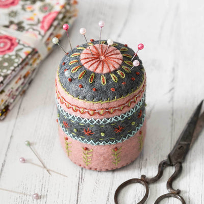 Decorative pincushion with embroidered patterns, pins, and a pair of scissors on a wooden surface. Pincushion Felt Craft Mini Kit – Complete DIY sewing kit with felt, thread, needle, stuffing, and instructions to make a handmade felt pincushion