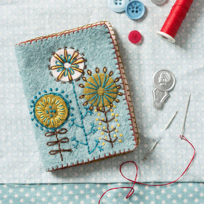 Embroidered notebook with floral designs on a tablecloth with sewing 
supplies. Needle Case Felt Craft Mini Kit – Complete DIY sewing kit with felt, thread, needle, stuffing, and instructions to make a handmade needle case