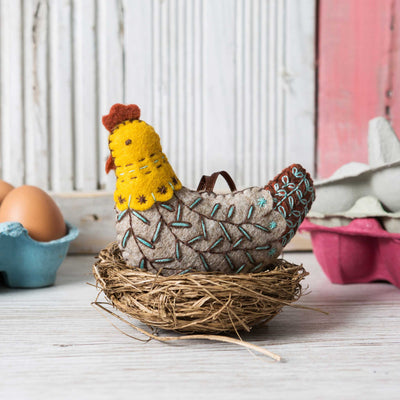 Felt rooster in a nest with eggs on a wooden surface Corinne Lapierre French Hen Felt Craft Kit – complete wool felt sewing kit with materials and instructions to hand-stitch a folk-style French Hen decoration