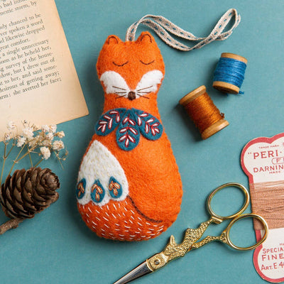 Stuffed fox toy with embroidery on a blue background with sewing  Corinne Lapierre Folk Fox Felt Craft Kit – complete wool felt sewing kit with materials and instructions to hand-stitch a folk-inspired fox decorationmaterials.