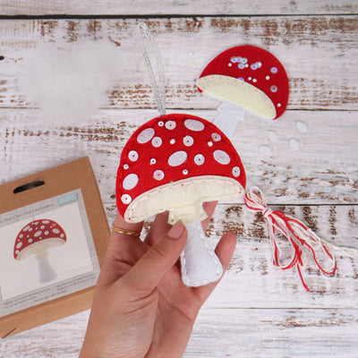 Red and white polka dot mushroom ornament held by a hand on a wooden surface. Toadstool – Felt Decoration Kit (SKU GCK224) with pre-cut red and white felt shapes, thread, needle, and stuffing for making a handmade woodland ornament, finished size approx. 10.5 x 13.5cm. Do not wash.