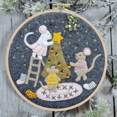 Embroidery hoop with festive scene of mice around a Christmas tree on a wooden background. Christmas with the Mouse Family Felt Appliqué Hoop Kit – Complete DIY sewing kit with felt, threads, hoop, needle, stuffing, and instructions to make a festive holiday decoration