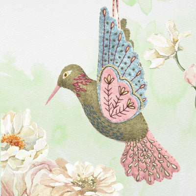 Hummingbird Felt Craft Mini Kit – Complete DIY sewing kit with felt, thread, needle, and instructions to make a colourful hummingbird decoration – SKU:MKHMB1F
Decorative embroidered hummingbird with floral patterns on a soft green background with flowers.